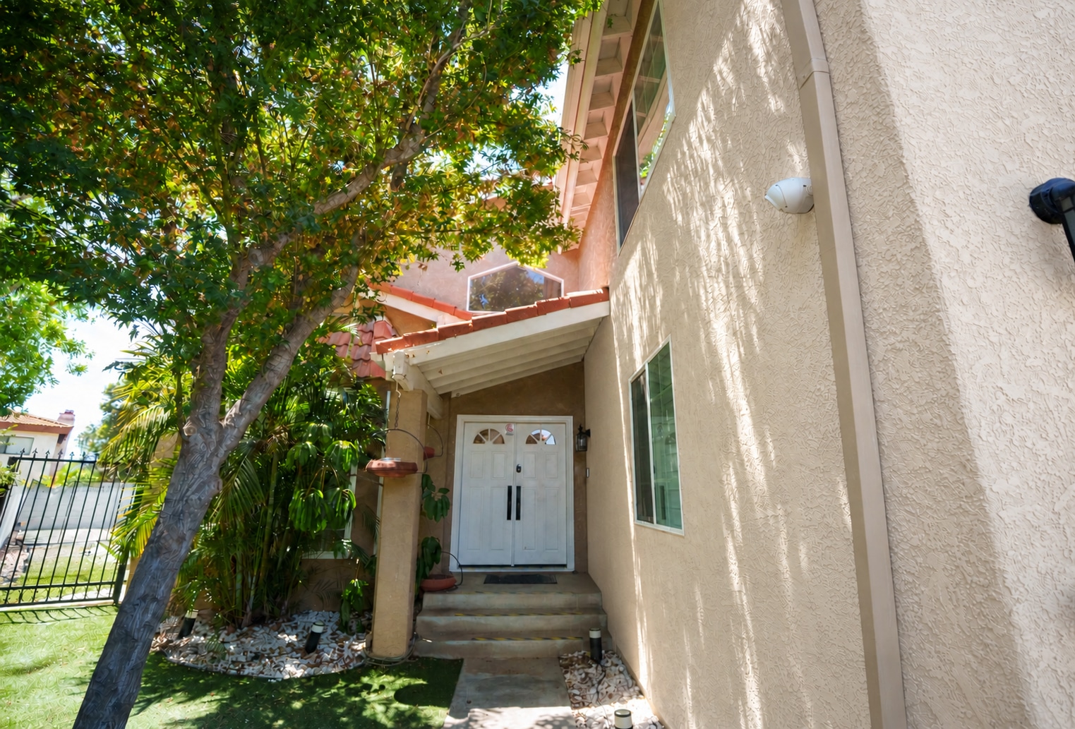 Covered residence entry with white double doors and a mature tree